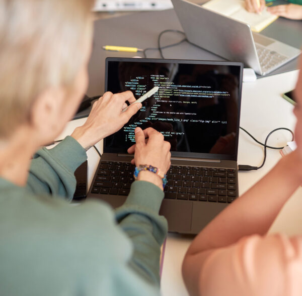 Focus on hands of young man with pen pointing at laptop screen with coded data while making presentation to classmate and explaining it