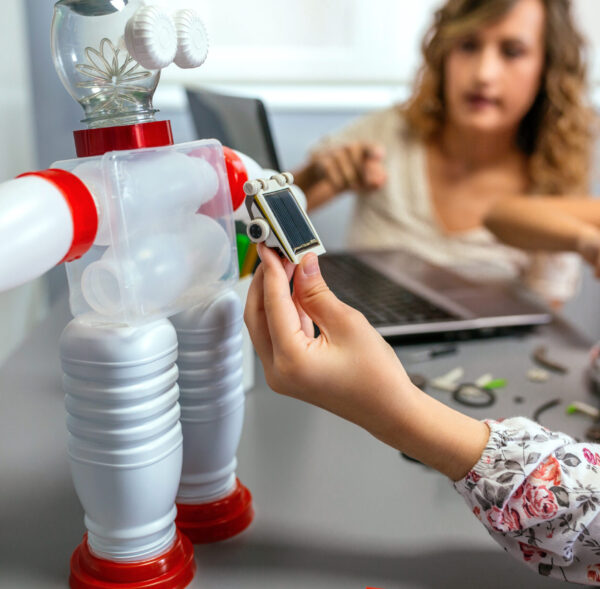 Female student holding solar panel over recycled toy robot made with plastic packages in a robotics class. Sustainable technological education concept.