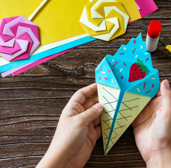 In the hands of a child origami paper ice cream on a wooden table. Children's art project, handmade, crafts for children.