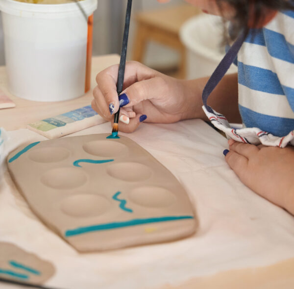 Woman painting and decorating a pottery in a ceramic workshop. Craft, art and hobbies concept.
