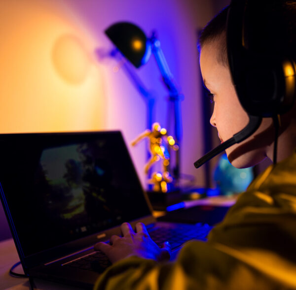 Young excited boy gamer with headphone playing video game on laptop at home.